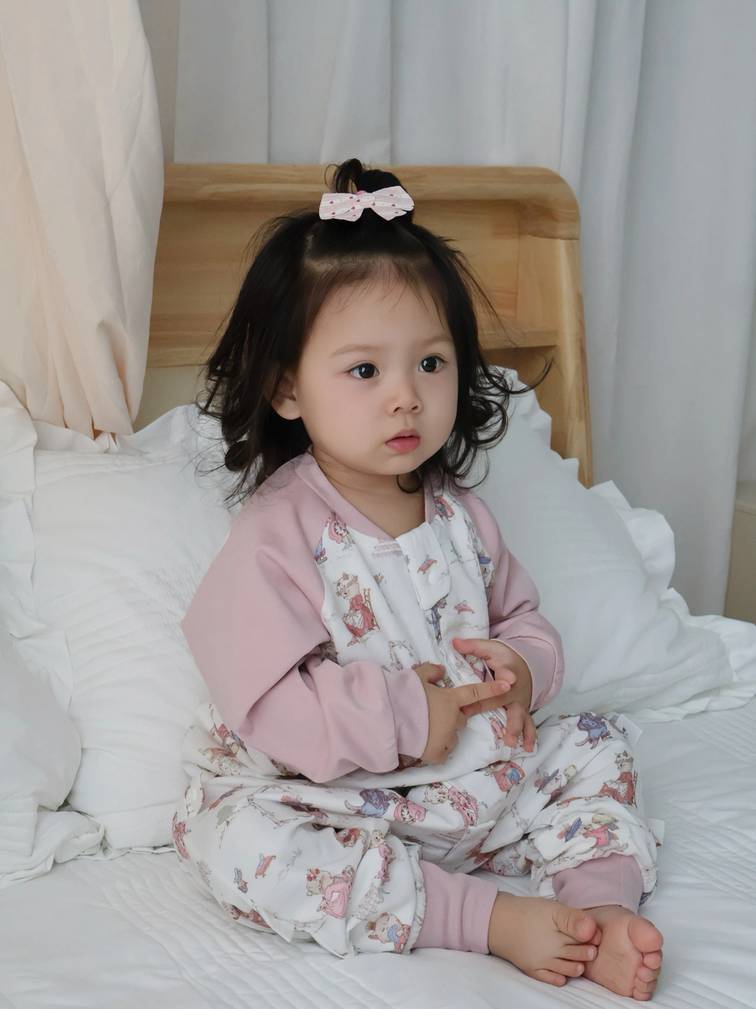 孩子穿着粉色睡袋坐在白色床铺上